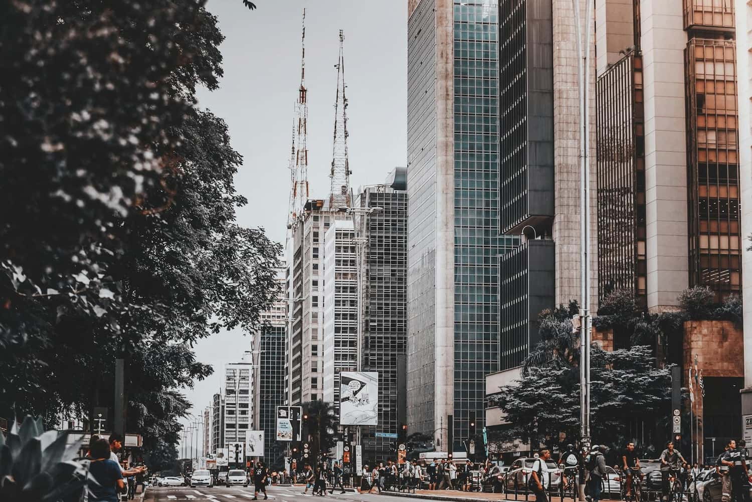 Fotografia na Vila Industrial de Campinas: uma avenida movimentada com pedestres e ciclistas em meio a prédios comerciais altos, retratando um ambiente urbano moderno similar ao dos melhores bairros para morar em Campinas.