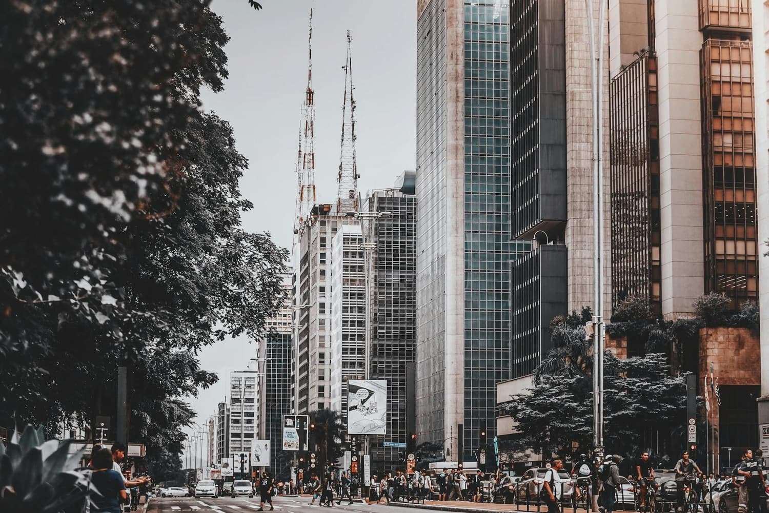 Fotografia na Vila Industrial de Campinas: uma avenida movimentada com pedestres e ciclistas em meio a prédios comerciais altos, retratando um ambiente urbano moderno similar ao dos melhores bairros para morar em Campinas.