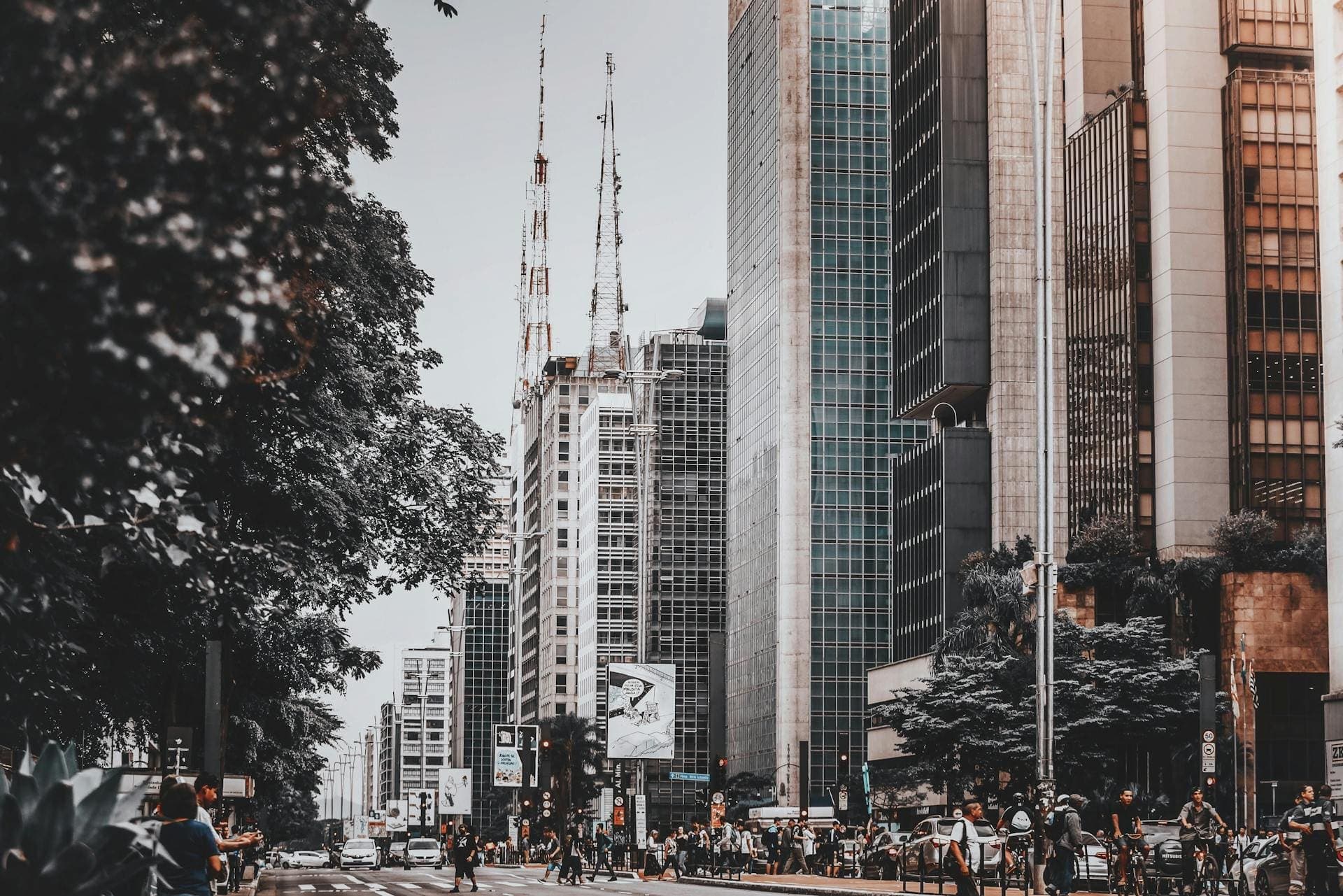 Fotografia na Vila Industrial de Campinas: uma avenida movimentada com pedestres e ciclistas em meio a prédios comerciais altos, retratando um ambiente urbano moderno similar ao dos melhores bairros para morar em Campinas.