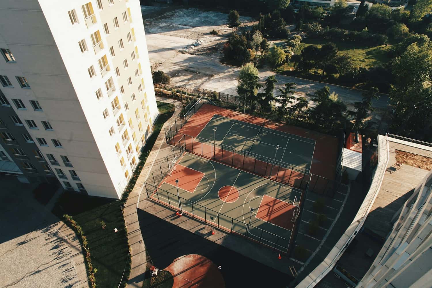 Vista aérea de uma quadra poliesportiva em condomínio residencial, cercada por prédios e áreas verdes ao fundo, ideal para lazer e atividades esportivas.